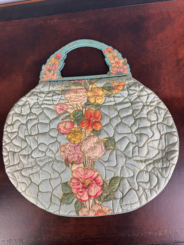 Antique quilted silk beach bag with hand‑painted wooden handles and floral appliqué.