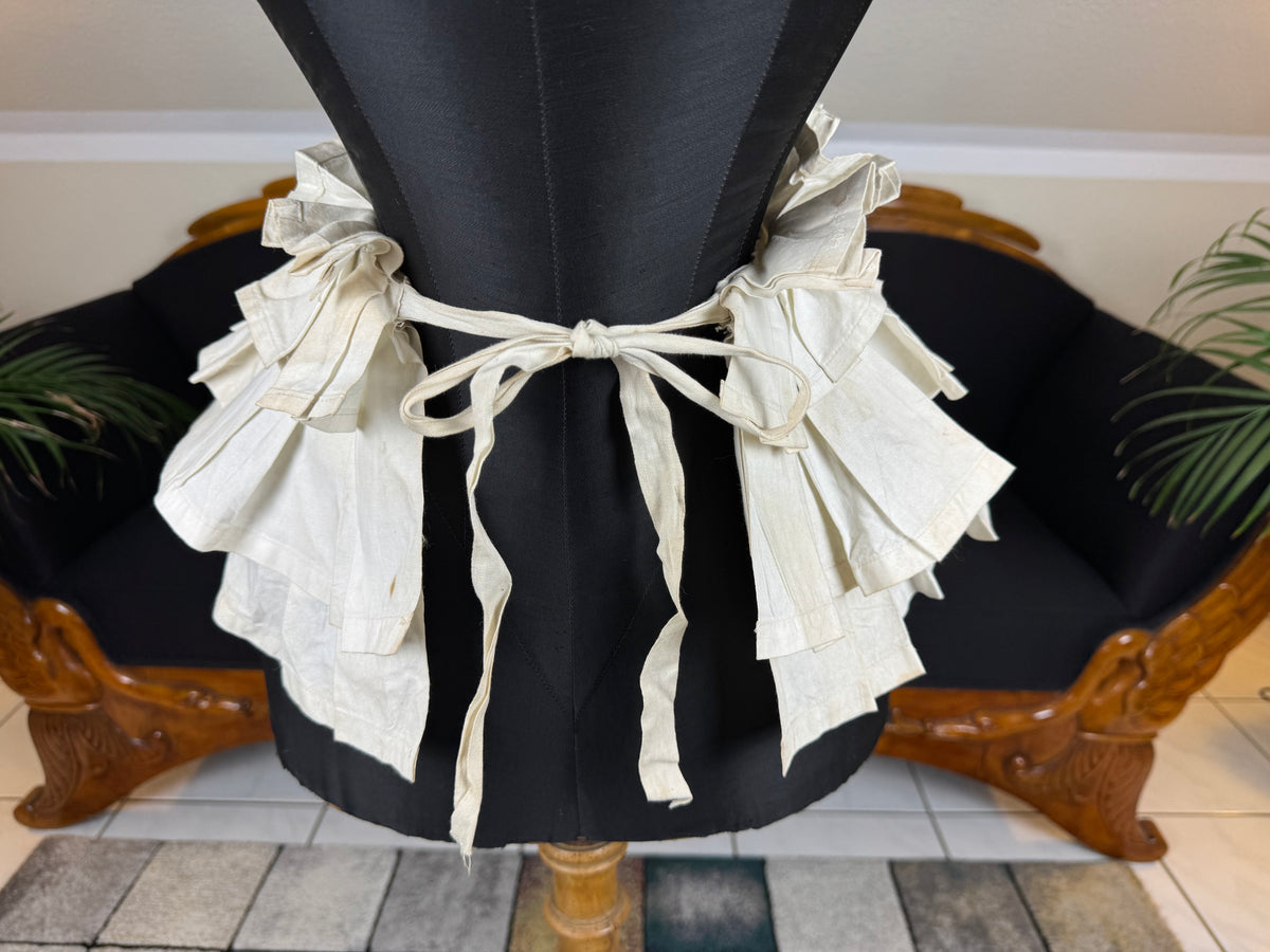 Victorian white linen four‑tier bustle pad c.1898 with pleated tiers and cotton waist tie.