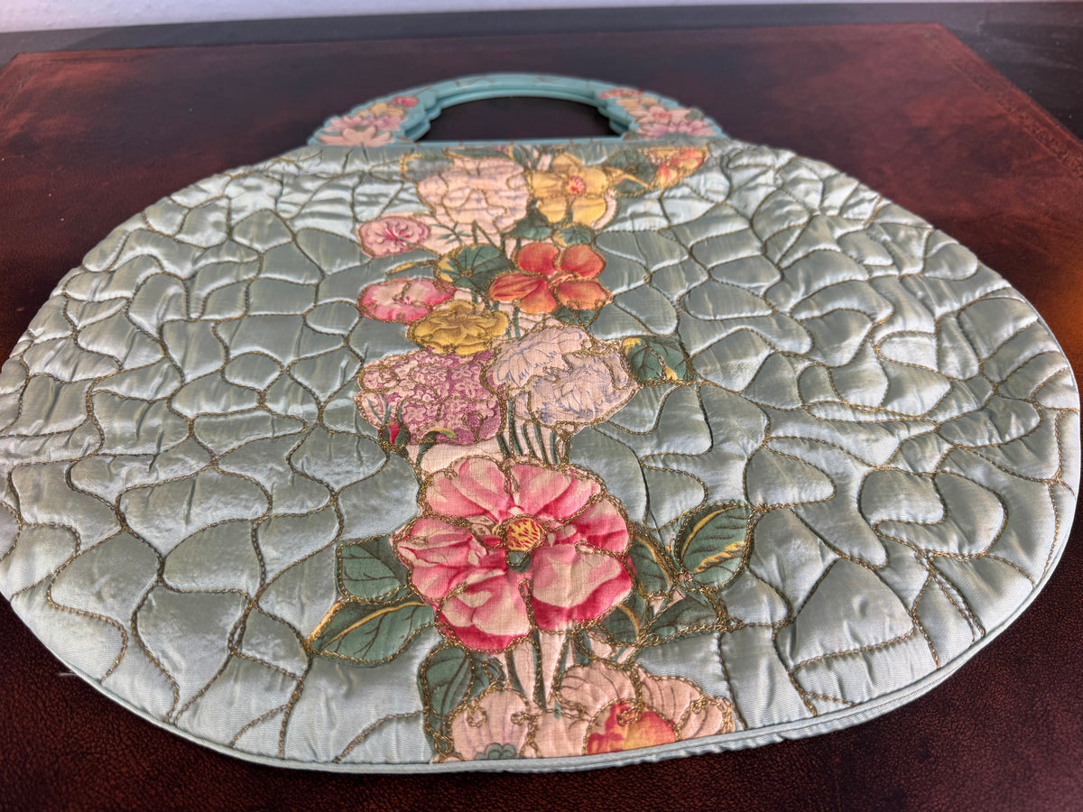 Antique quilted silk beach bag with hand‑painted wooden handles and floral appliqué.