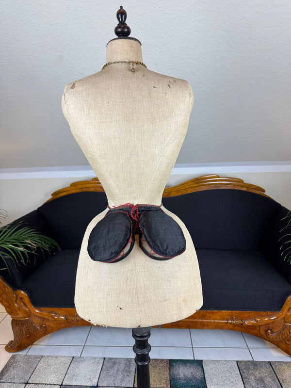 Victorian V.C.B spring frame skirt pad c.1895 with black silk covering, red trims and wire‑frame folding oval construction.