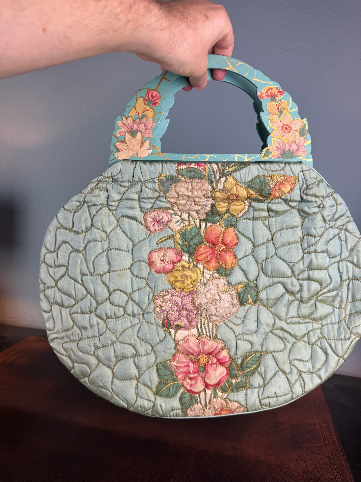 Antique quilted silk beach bag with hand‑painted wooden handles and floral appliqué.