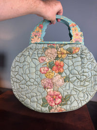 Antique quilted silk beach bag with hand‑painted wooden handles and floral appliqué.